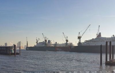 Cranes at harbor against sky in city