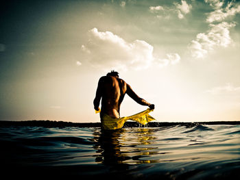 Side view of shirtless man standing in sea against sky