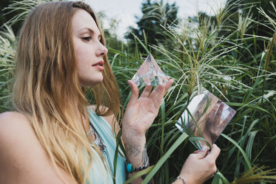 Young woman holding prism and mirror while standing against plant