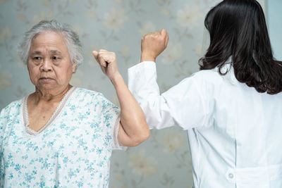 Senior woman and doctor touching elbows at home