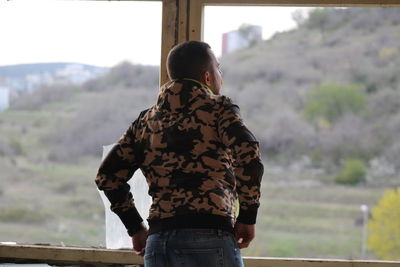 Rear view of man watching outside a broken window 