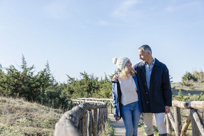 Man with arm around woman standing on wooden bridge