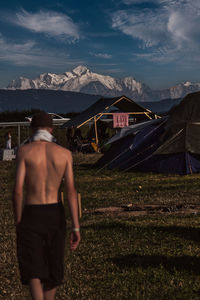 Rear view of shirtless man standing on field against sky