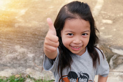 Portrait of smiling girl showing thumbs up while standing outdoors