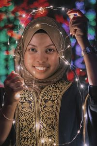 Portrait of smiling young woman holding illuminated lighting equipment at night