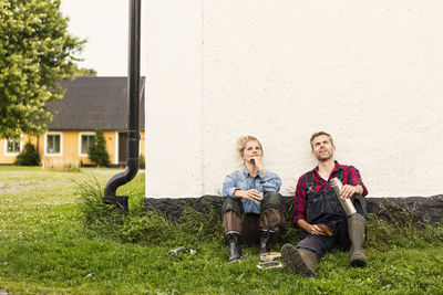 Man and woman relaxing while looking up against house