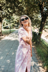 Portrait of smiling young woman wearing sunglasses standing on footpath