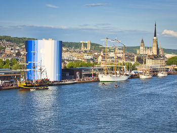 Sailboats in city by river against sky