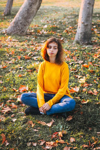 Curly young girl in yellow sweater and jeans sitting on fall grass with dry leaves. autumn mood