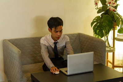 Young man using laptop while standing against wall