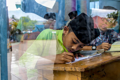 Boys studying at table seen through window