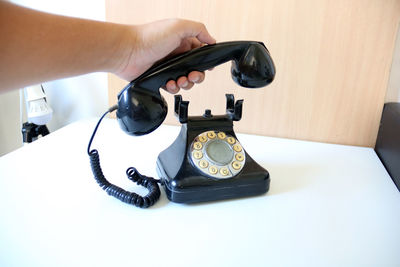 Close-up of hand holding receiver of old landline phone on table