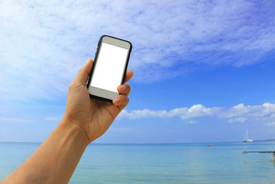 Close-up of hand holding smart phone against blue sky