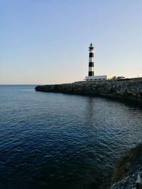 Lighthouse by sea against clear sky