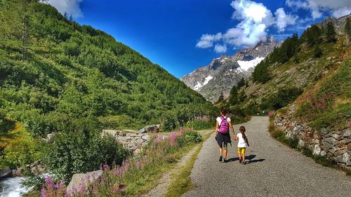 Rear view of woman walking with daughter on mountain road