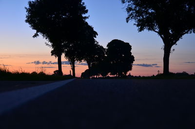 Silhouette tree by road against sky during sunset