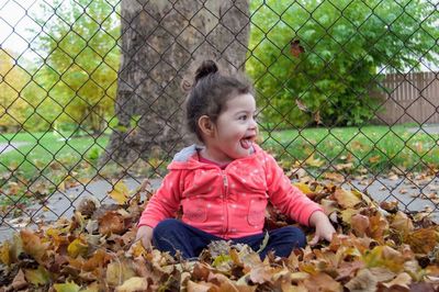 Girl playing with autumn leaves against fence in park