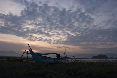 Boat moored on field against sky during sunset