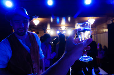 Cropped image of hand holding wineglass with friends during party in background