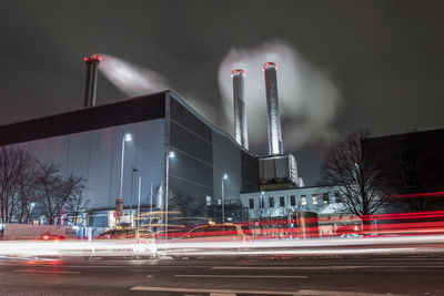 Light trail on street by smoke stacks emitting pollution