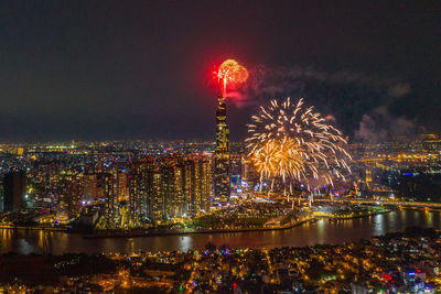 Firework display over river with illuminated buildings in background