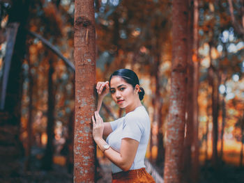 Portrait of young woman standing on tree trunk