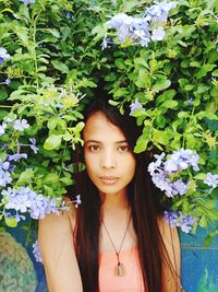 Portrait of beautiful young woman standing by flowering plant