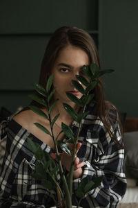 Portrait of young woman with plant sitting at home