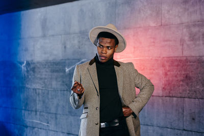 Young man looking away while standing against wall