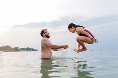Side view at girl full of splashes jumping in the water from the father arms