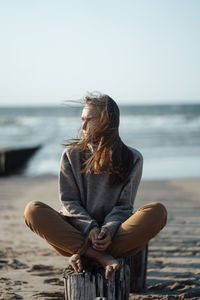 Young woman sitting on wooden post at beach