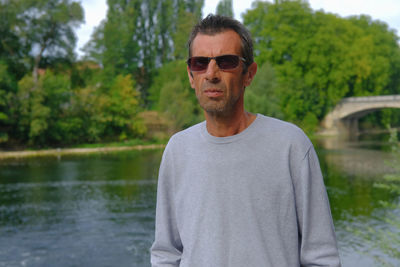 Portrait of man standing by lake against trees