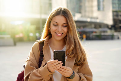 Smiling woman using mobile phone on street