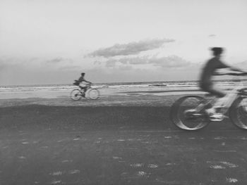 People riding bicycle on beach against sky