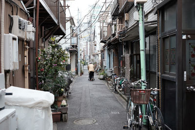 Rear view of woman walking on alley amidst buildings in city