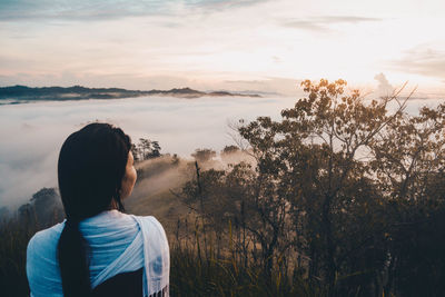 Rear view of woman looking at foggy landscape during sunset