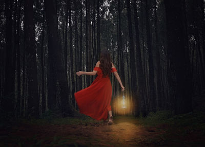 Rear view of woman with old lantern walking against trees in forest