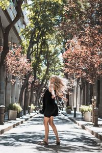 Full length of woman standing by flowering tree in city