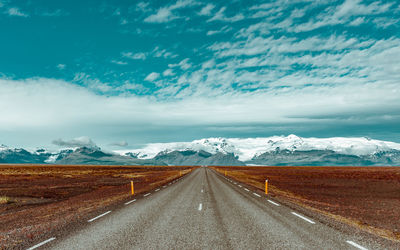 Empty road leading towards mountains against sky