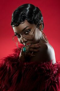 Young woman wearing eyeglasses and fur clothing standing against red background