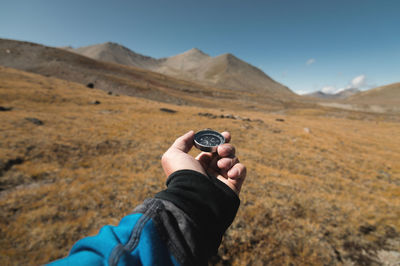 First-person view of a male traveler's hand holding a magnetic compass against the backdrop 