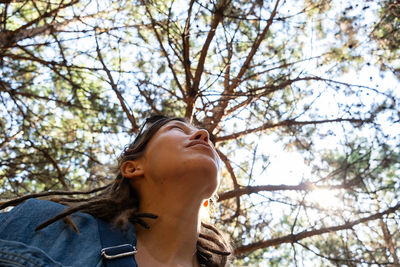 Woman looking up through the trees in the summery forest.