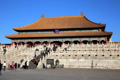 Tourists in front of temple against clear blue sky