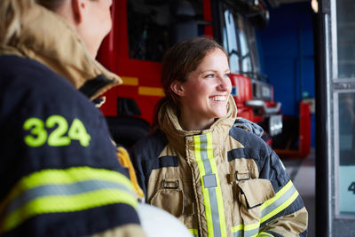 Smiling female firefighter standing with coworker in fire station