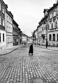 Senior woman walking on street amidst buildings against sky