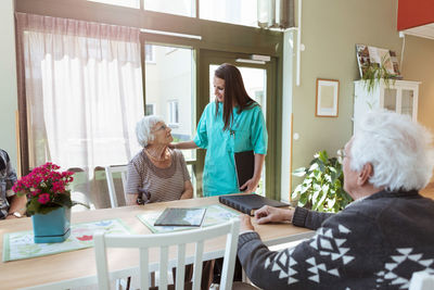 Young nurse talking with senior woman sitting at table in nursing home