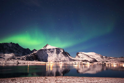 Stunning dancing northern lights over snowy mountains and sea coast in lofoten islands, norway. 