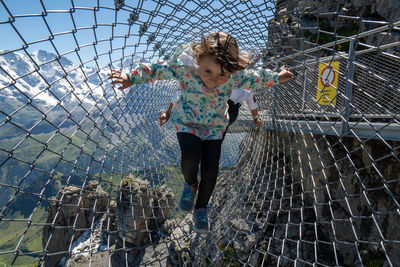 Full length of girl with arms raised against fence