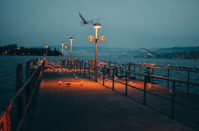 Illuminated pier over sea against clear sky