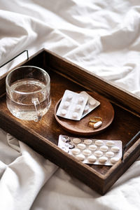 Wooden tray with pills, vitamins or supplements and water glass on the bed. 
